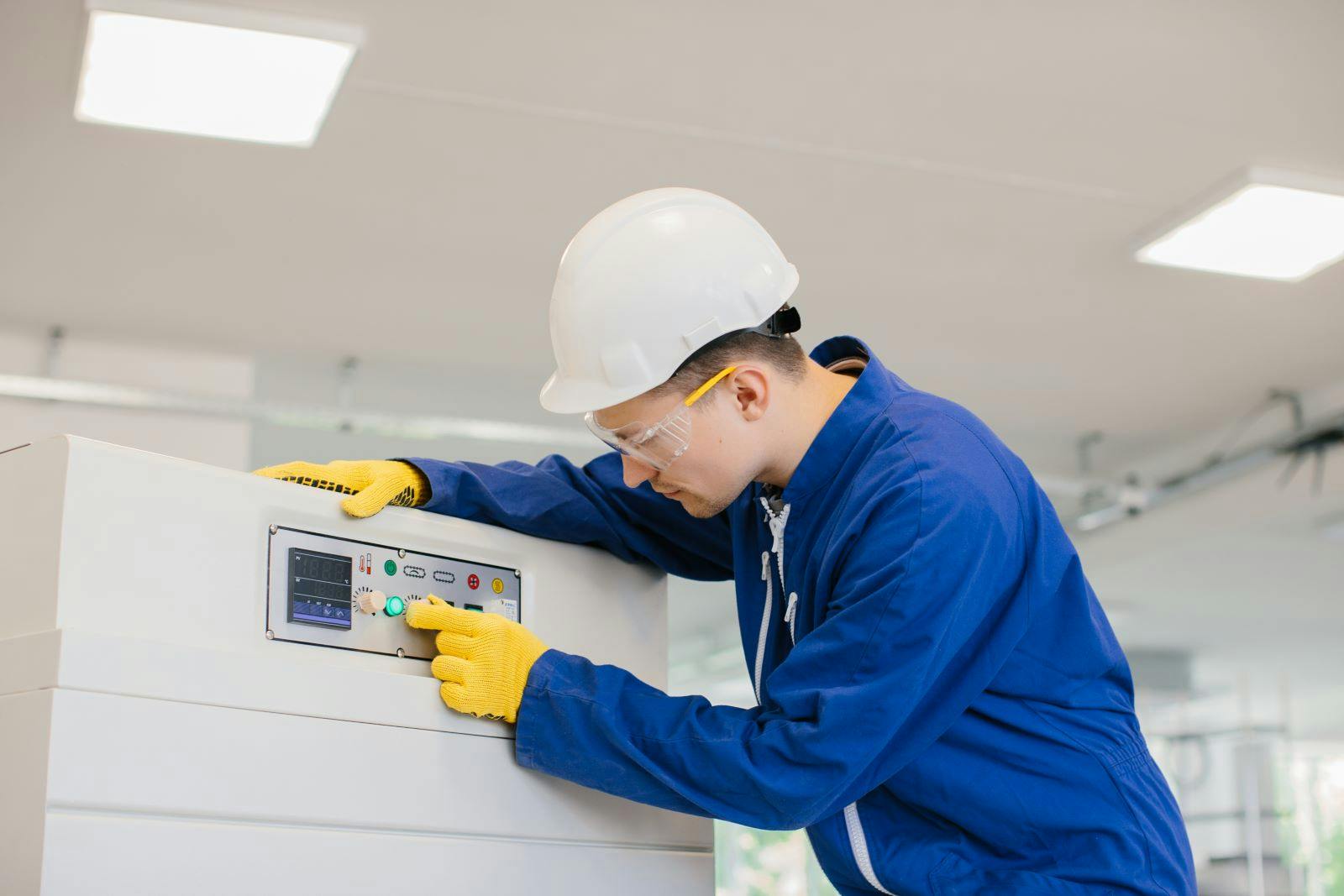 Industrial technician operating control panel, pushing button, wearing safety glasses, gloves, and helmet