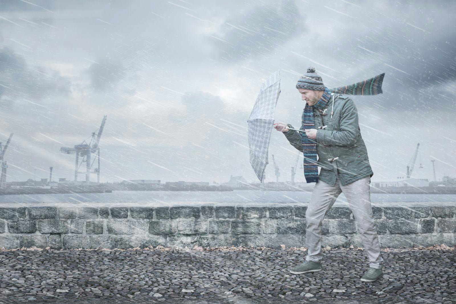 Pedestrian with an umbrella is facing strong wind and rain on a dockside