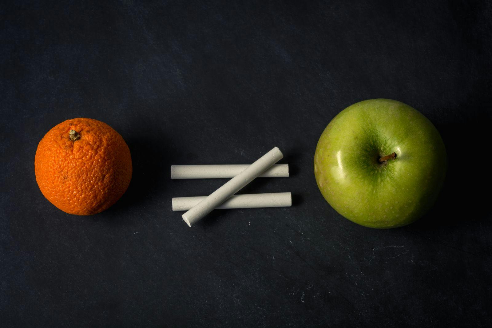 Orange does not equal apple with chalk on top of chalkboard suggesting inequality in different fruit