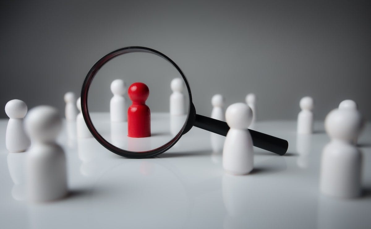 Black magnifying glass over red wooden figurine