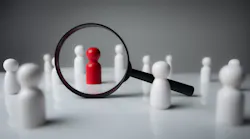 Black magnifying glass over red wooden figurine Black magnifying glass over red wooden figurine