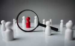 Black magnifying glass over red wooden figurine Black magnifying glass over red wooden figurine