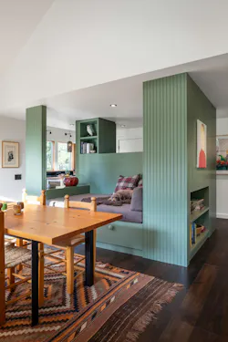 A small dog lays on the daybed in this contemporary cabin. In front of him is a wooden dining table. A small dog lays on the daybed in this contemporary cabin. In front of him is a wooden dining table.