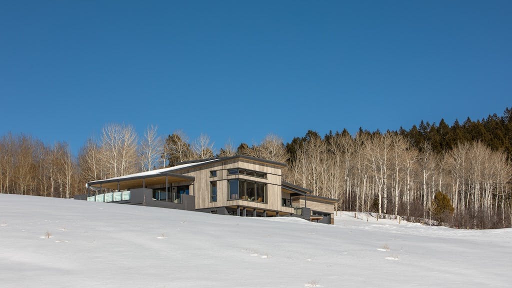 A contemporary home sits in a snowy hillside.