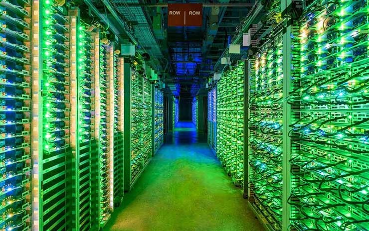 The blinking lights of racks of Google servers glow in a darkened data hall in St. Ghislain, Belgium. (Image: Google)