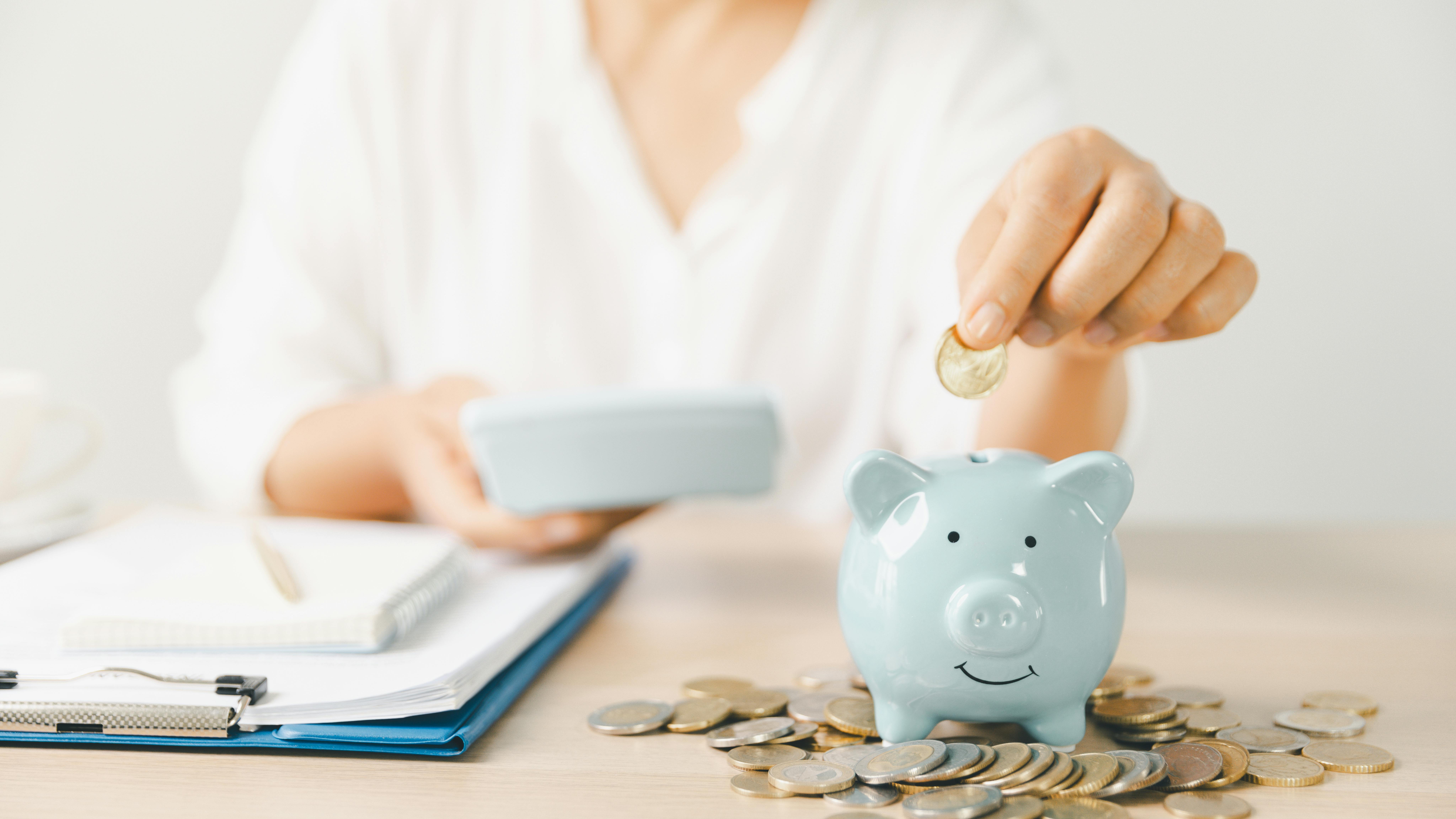 Woman sitting at desk, putting coin into piggy bank