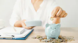 Woman sitting at desk, putting coin into piggy bank Woman sitting at desk, putting coin into piggy bank