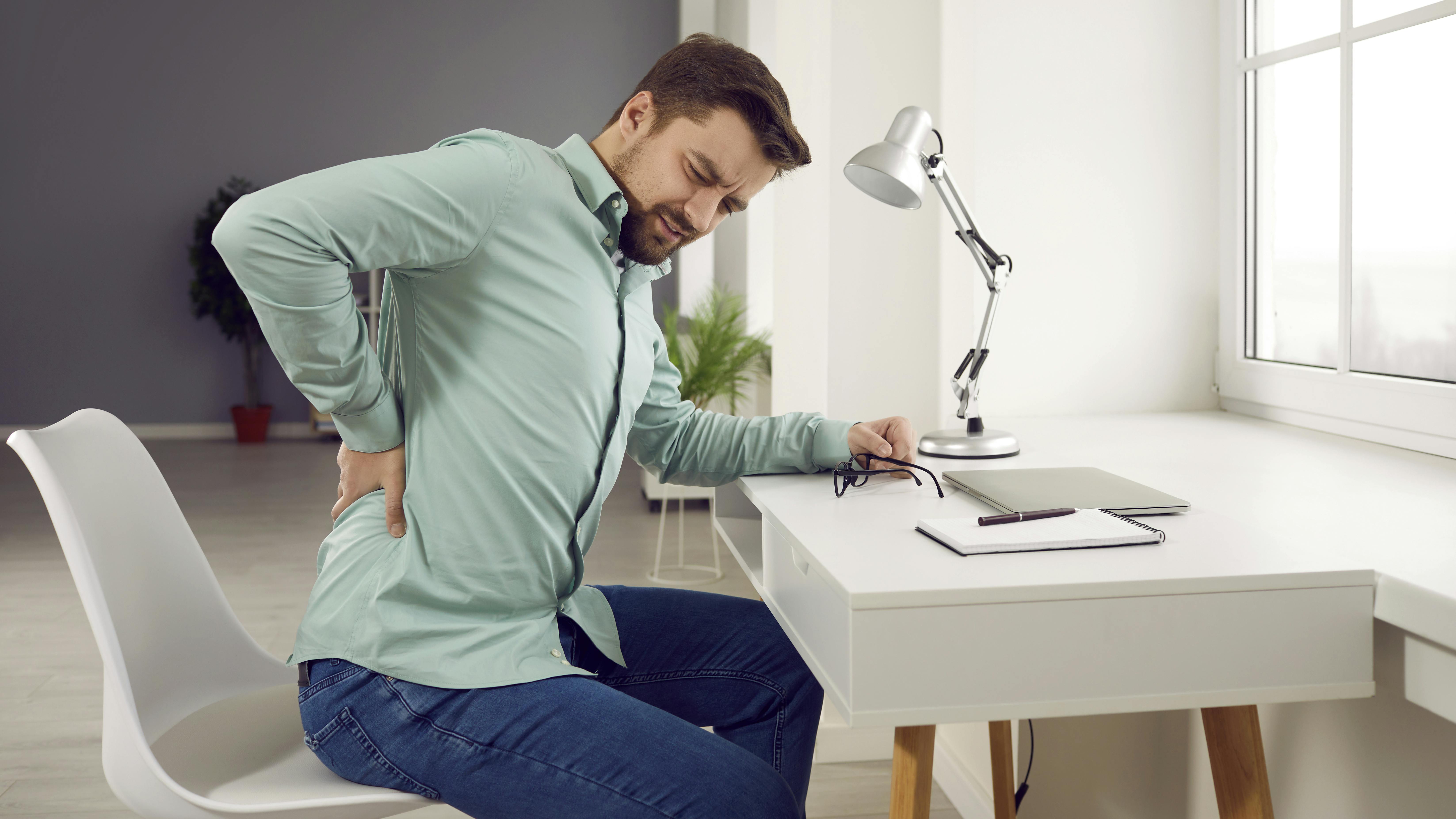 man sitting at a desk rubbing his sore back