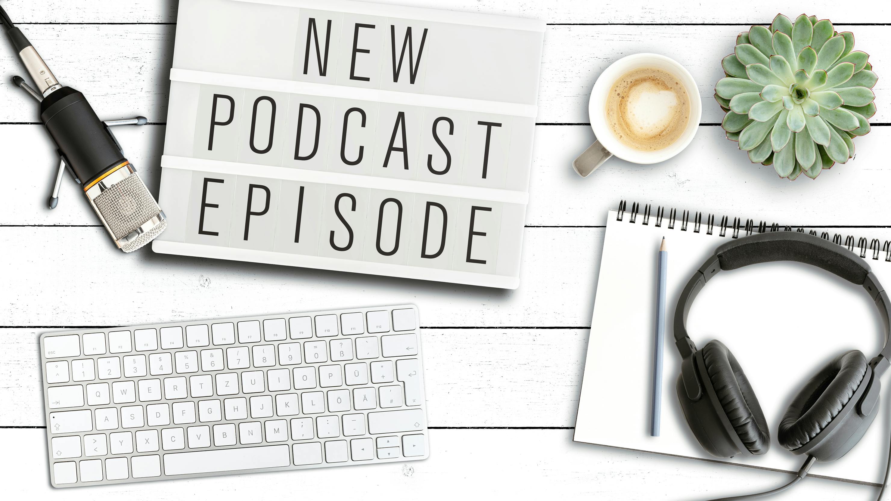 Podcasting concept, top view of words NEW PODCAST EPISODE on light box on table with microphone and computer keyboard