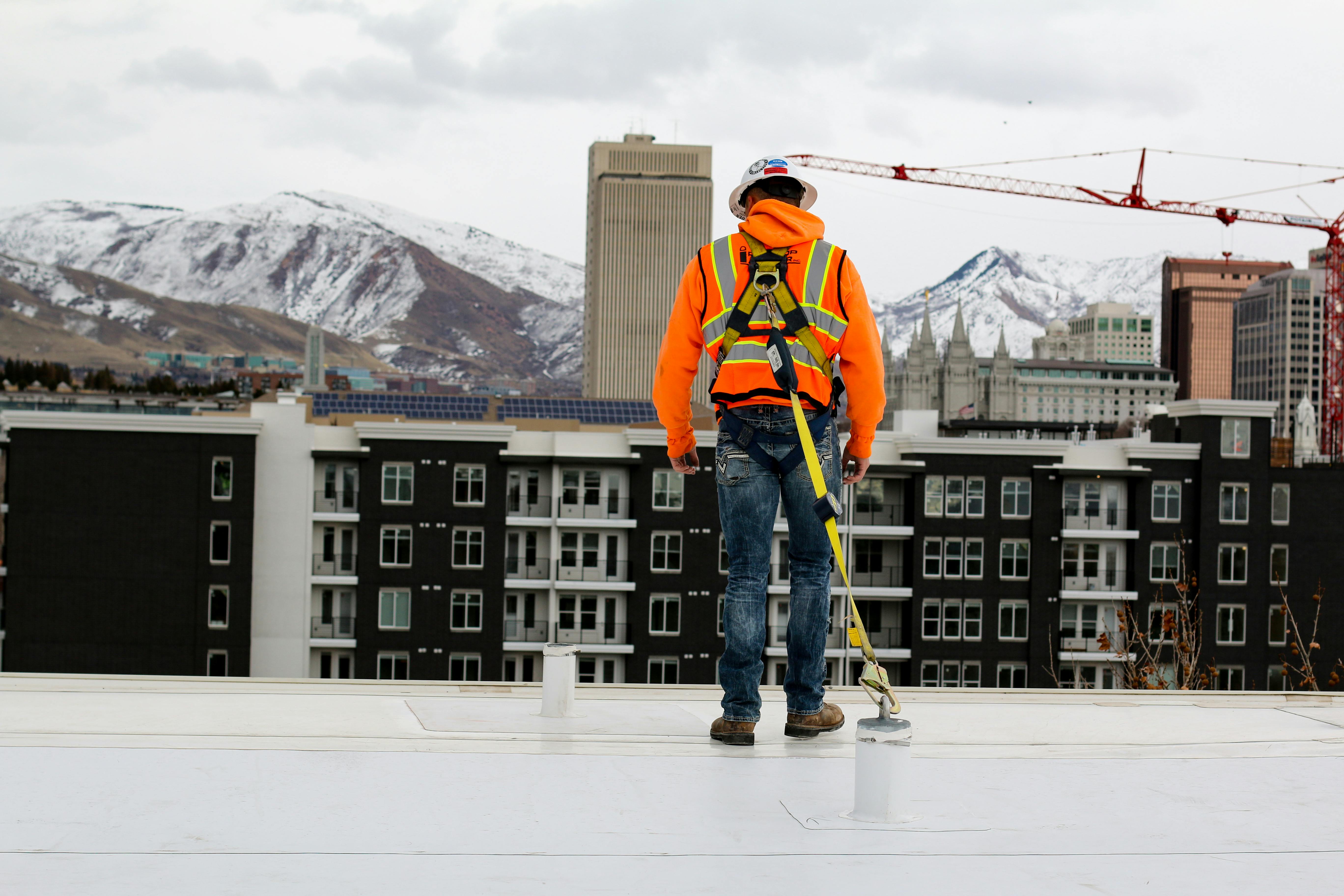 worker standing on a ledge tethered with fall protection PPE overlooking housing complex and mountains