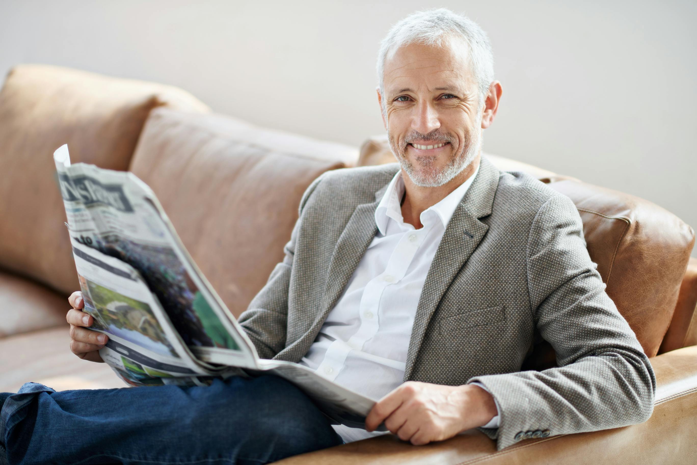 older man in sport coat reading a newspaper and smiling