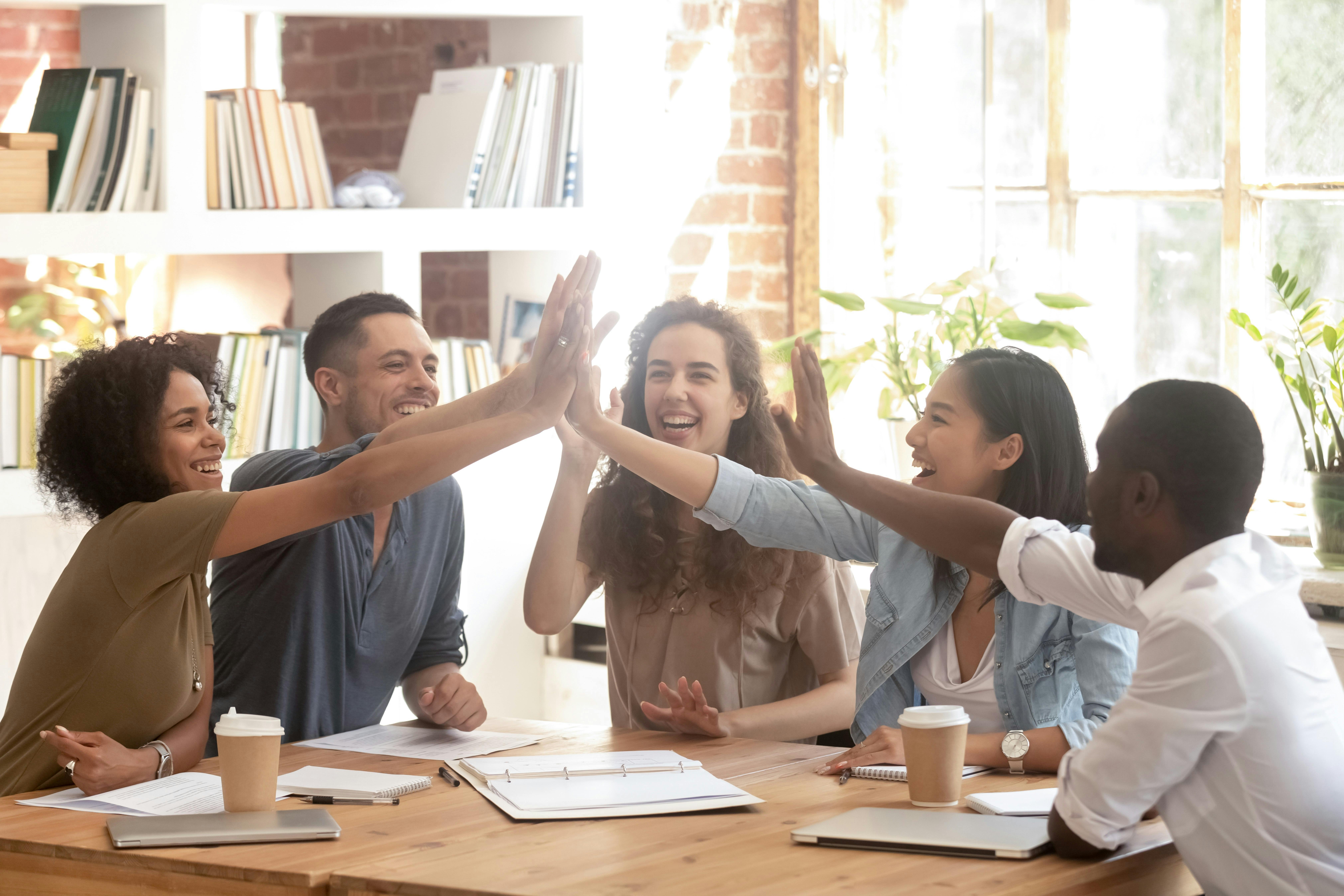 5 co-workers sitting around a table clapping their hands as a sign of teamwork and comraderie