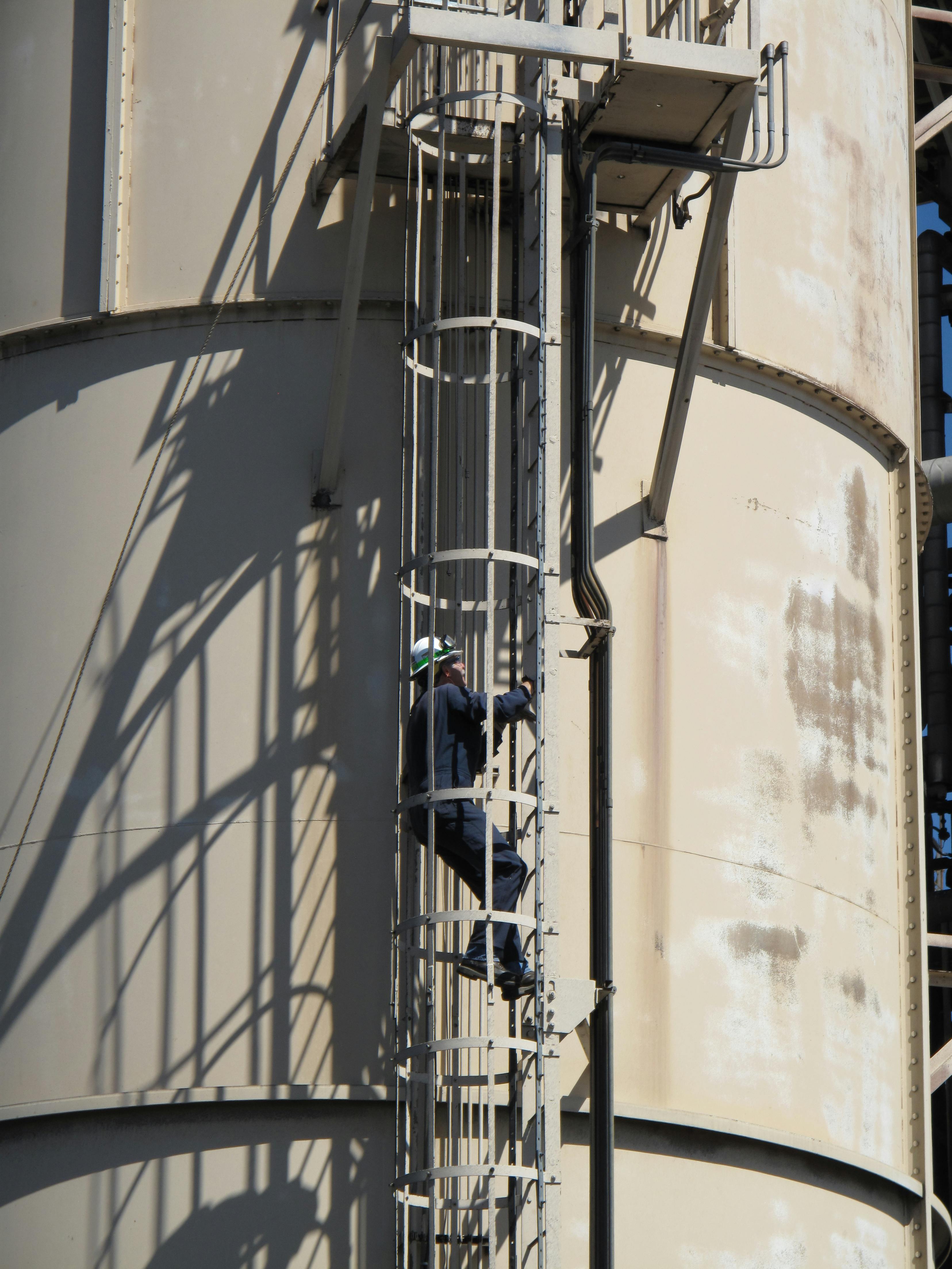 Photo of a worker climbing a caged ladder on the exterior of a metal structure