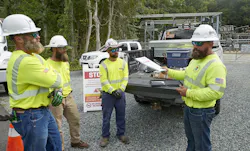 four tradesmen wearing safety helmets and hi-visibility shirts out in the field during a standup meeting four tradesmen wearing safety helmets and hi-visibility shirts out in the field during a standup meeting
