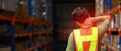 worker in a warehouse wearing a hi-vis vest with his back to camera holding his neck in pain worker in a warehouse wearing a hi-vis vest with his back to camera holding his neck in pain