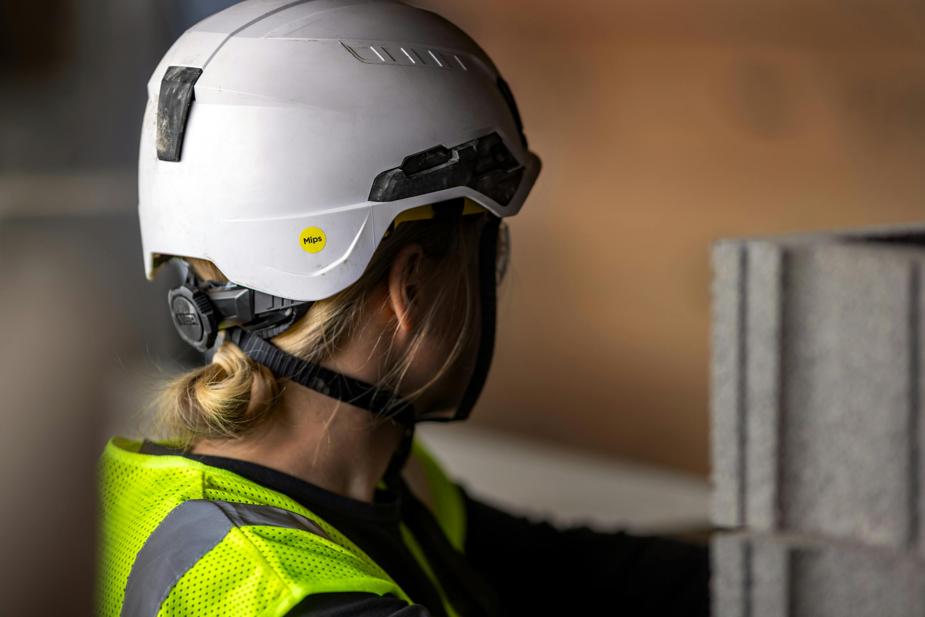 Picture of a woman in a hi-vis safety vest and Mips Type 2 safety helmet at a construction site looking away from the camera