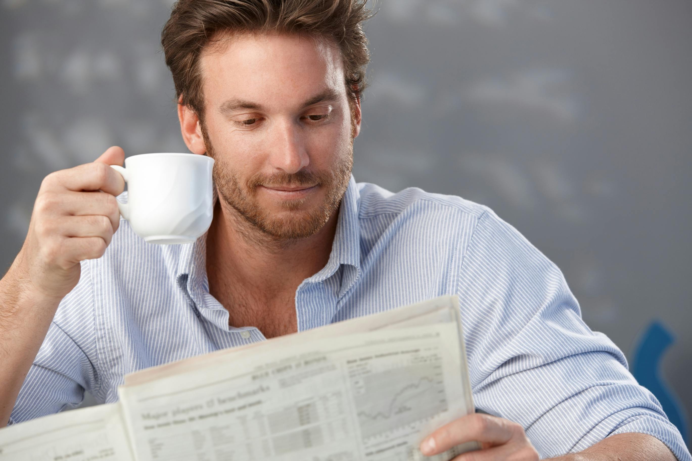 man sitting and holding an espresso cup in one hand and the newspaper in another
