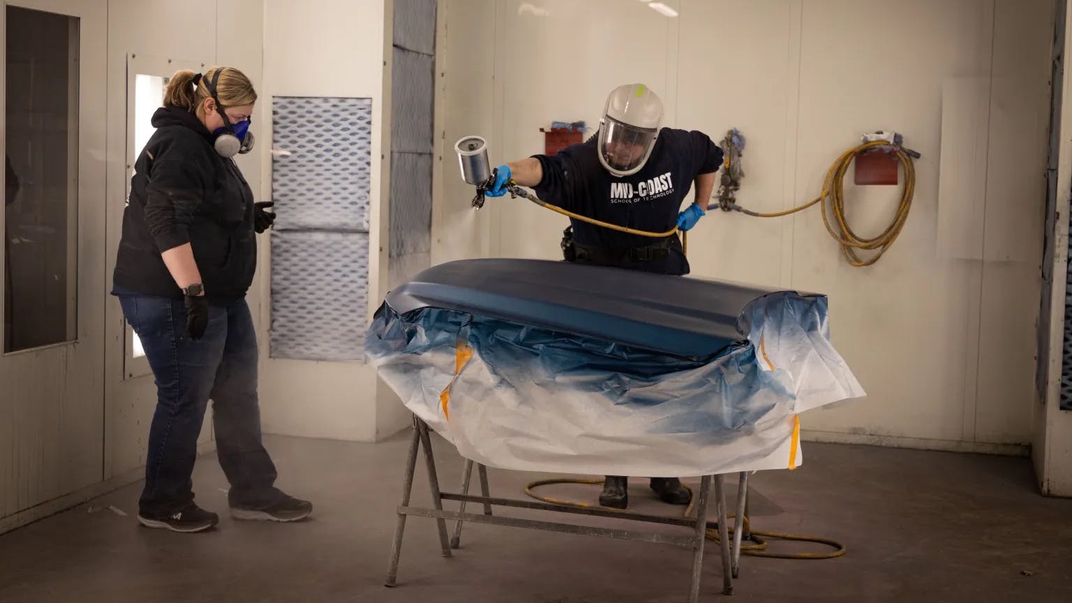 Danica Wooster working with MCST student Andrew Zuidema refinishing a hood in the paint booth.