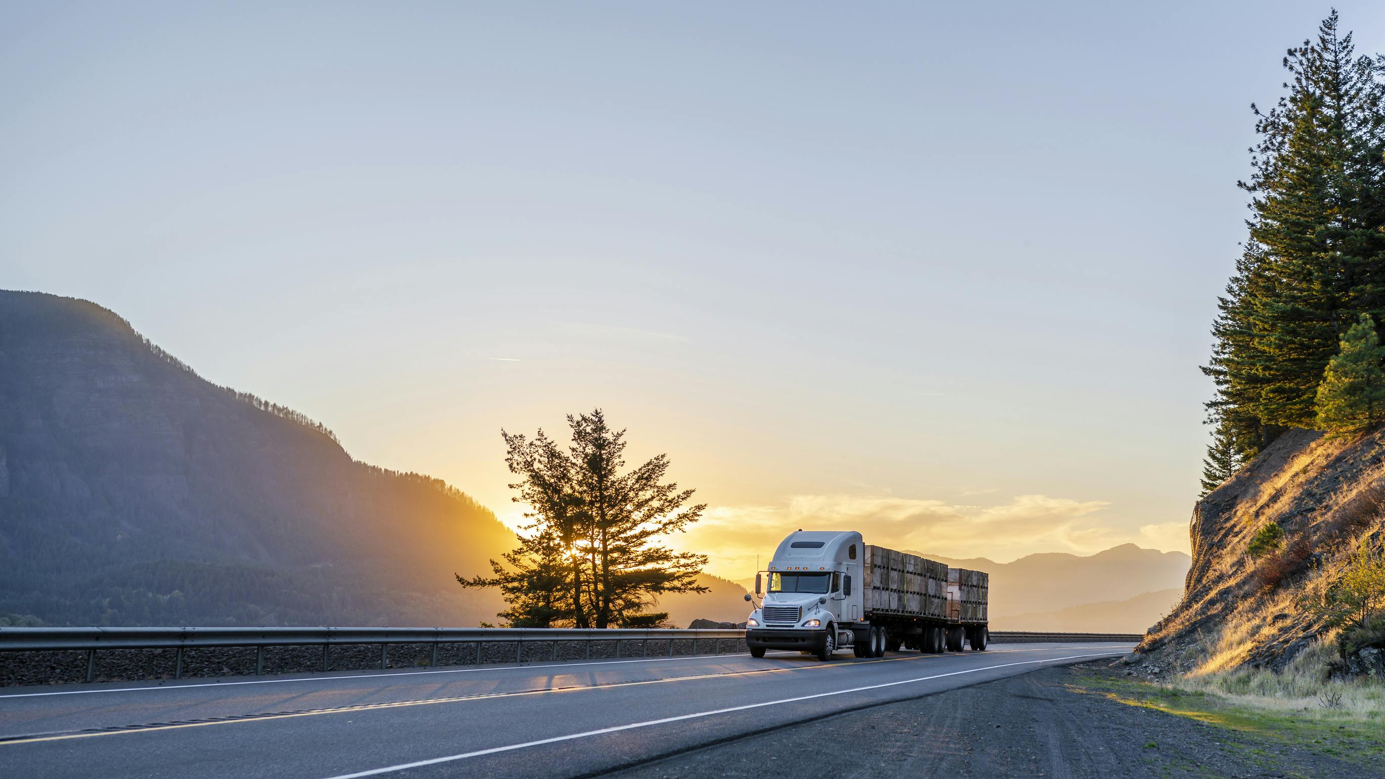 White big rig semi truck transporting boxes of apples on a flatbed trailer during evening on a U.S. highway for long-haul freight delivery