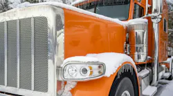 A classic orange big rig semi-truck with an extended cab parked in a snowy and icy truck stop parking lot during winter. A classic orange big rig semi-truck with an extended cab parked in a snowy and icy truck stop parking lot during winter.