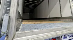 A view looking into the empty cargo space of a new commercial dry van trailer from the open rear doors, featuring a wooden floor, metal interior walls, and a diamond plate threshold. A view looking into the empty cargo space of a new commercial dry van trailer from the open rear doors, featuring a wooden floor, metal interior walls, and a diamond plate threshold.