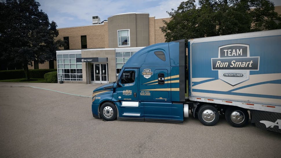 A blue and yellow Albert Transport Freightliner Cascadia truck pulling a Team Run Smart trailer.
