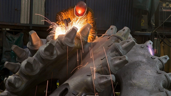 A worker at ESCOrsquos Main Plant in Portland uses an angle grinder to finish a cutting head for a dredging machine head