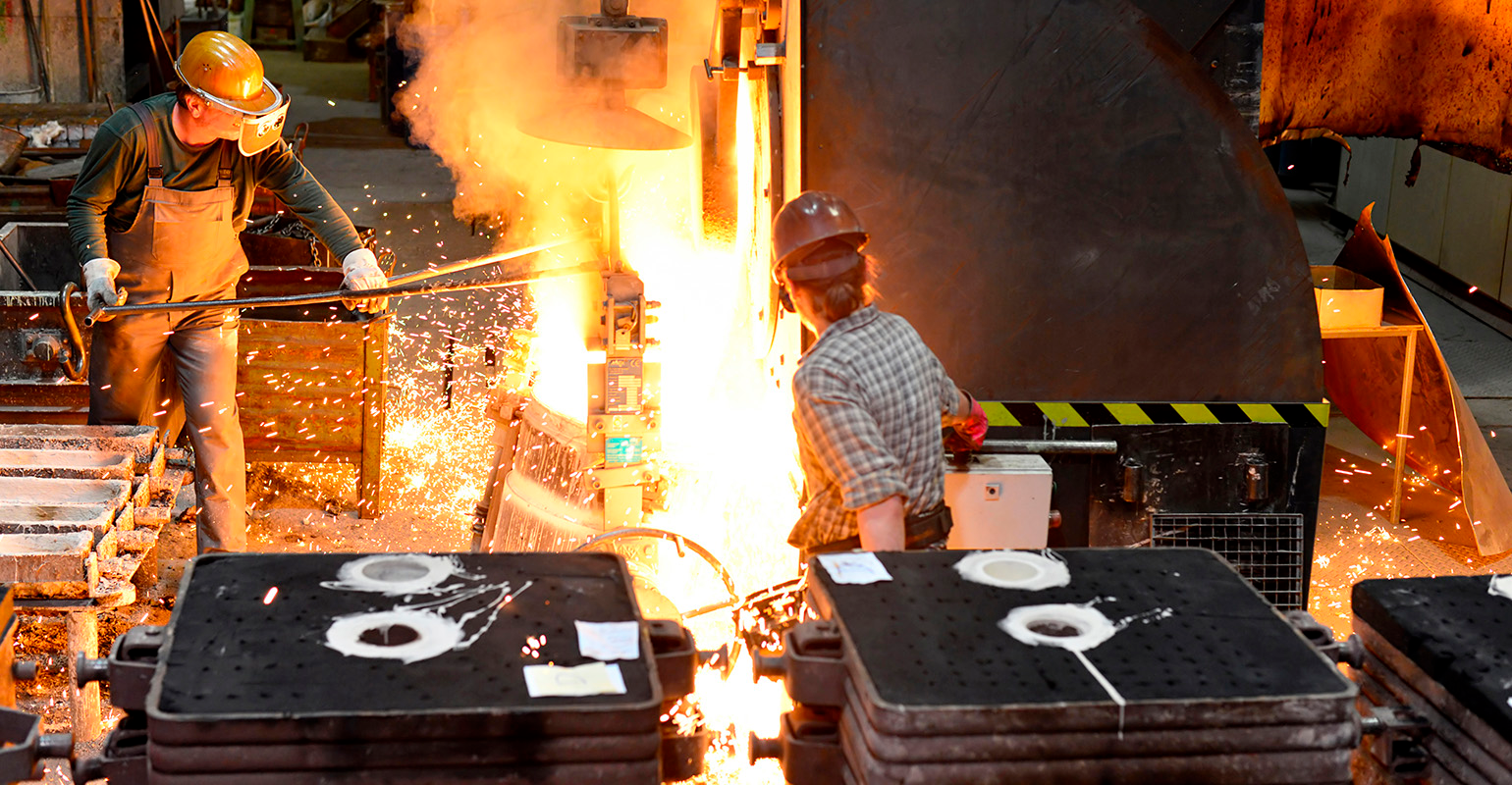 Workers in a foundry casting a metal workpiece.