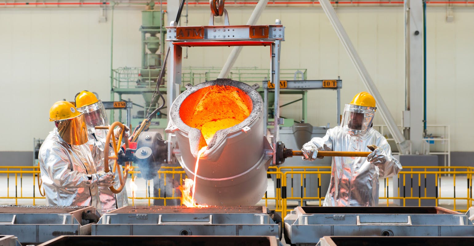 Workers pouring molten metal into sand molds.