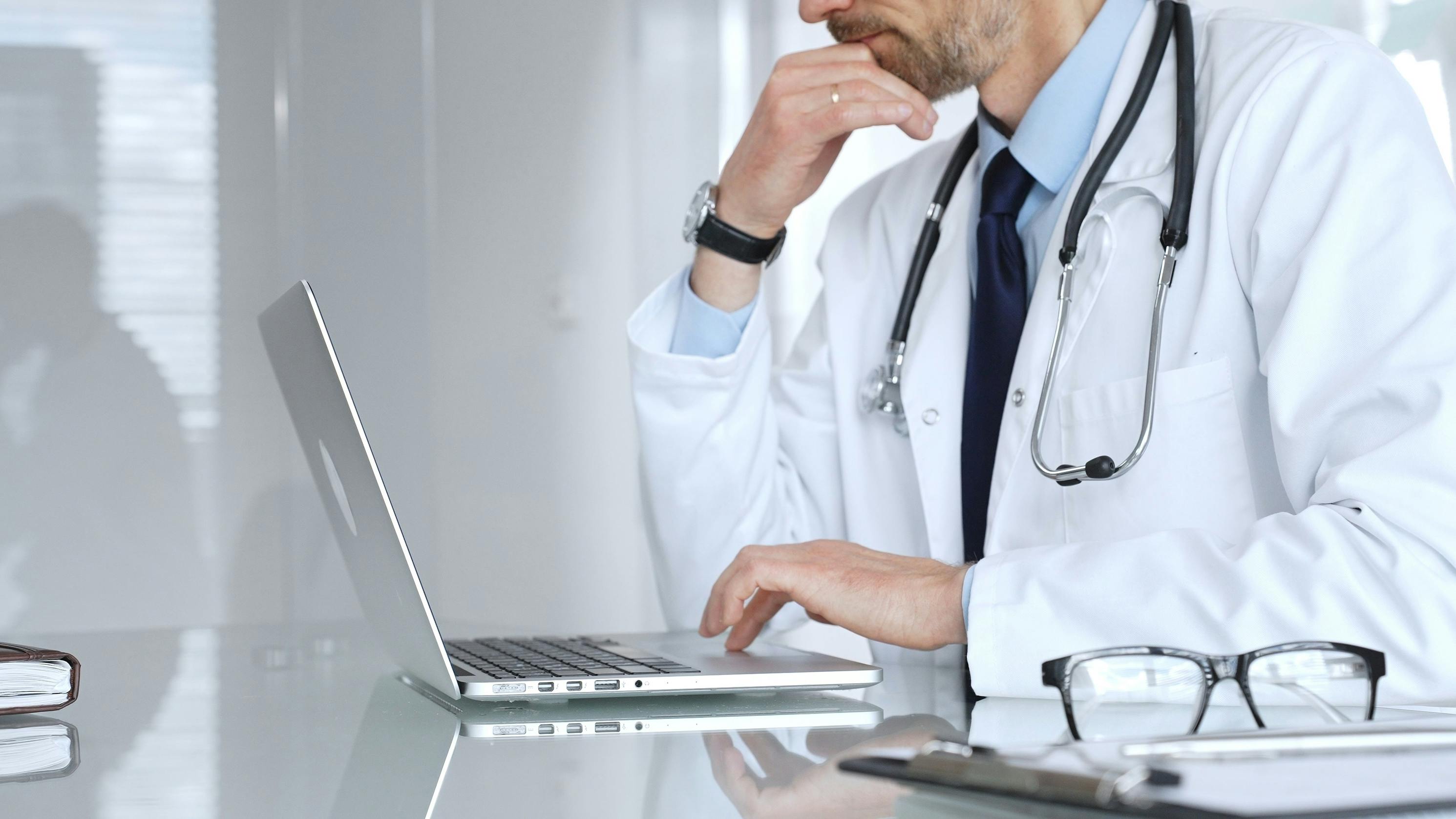 A doctor working on a laptop in a medical office focusing on patient data and healthcare documentation.