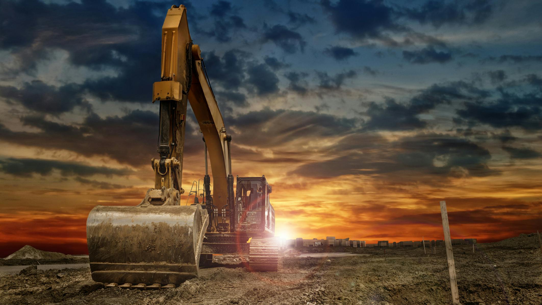 An excavator at a construction site with the sun rising behind it