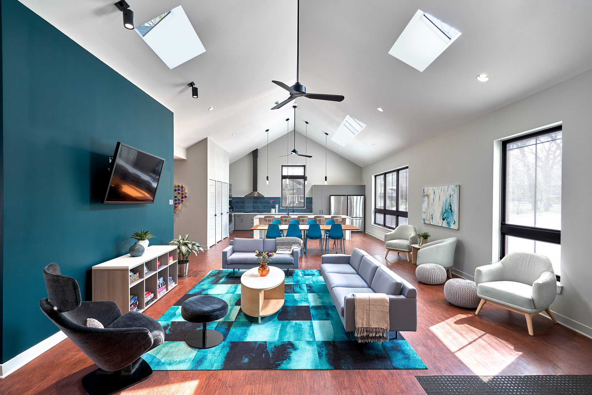 The design turned a formerly dark, dingy living room into a large, open, light-filled space thanks to the expansive windows and skylights, with rich, deep teal accents that extend from the great room to the kitchen beyond.