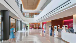 Two-story atrium lobby hospital entrance with wood ceilings and paneling against white balcony and check-in kiosks. Two-story atrium lobby hospital entrance with wood ceilings and paneling against white balcony and check-in kiosks.