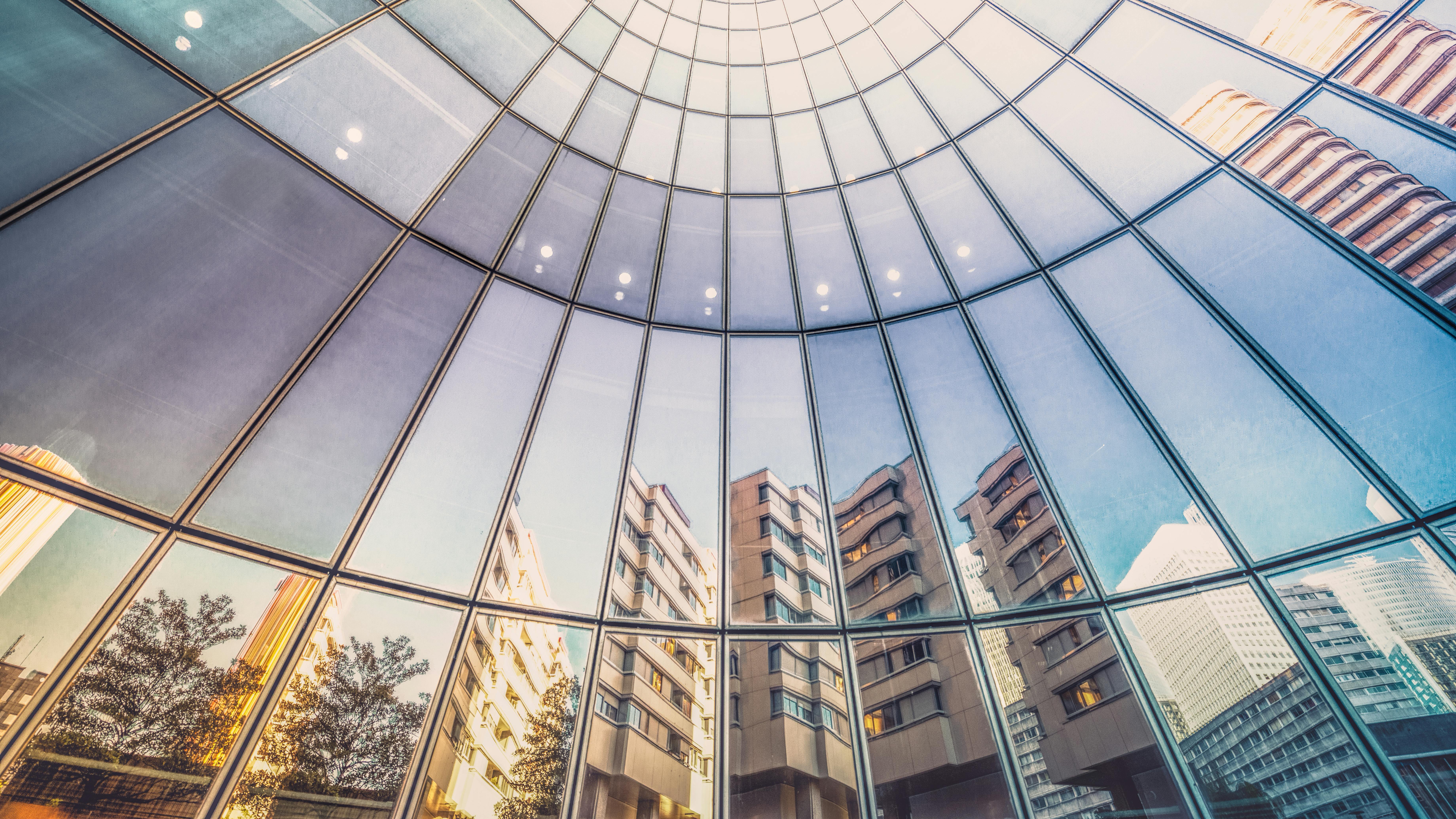 Reflection of apartment buildings in curved, glass facade of modern office tower.