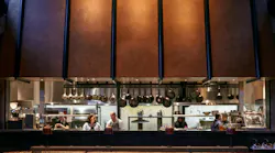 Amelia Gene's open kitchen with large, industrial looking cooper hood faces the main restaurant seating Amelia Gene's open kitchen with large, industrial looking cooper hood faces the main restaurant seating