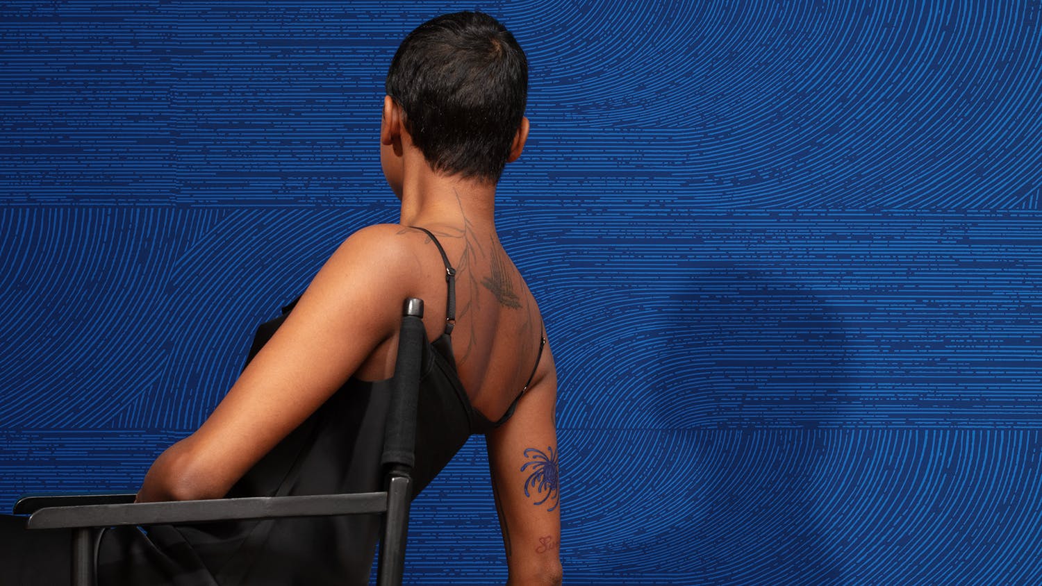 Person with back turned sitting in chair in front of deep blue wallcovering with intricate line patterns.