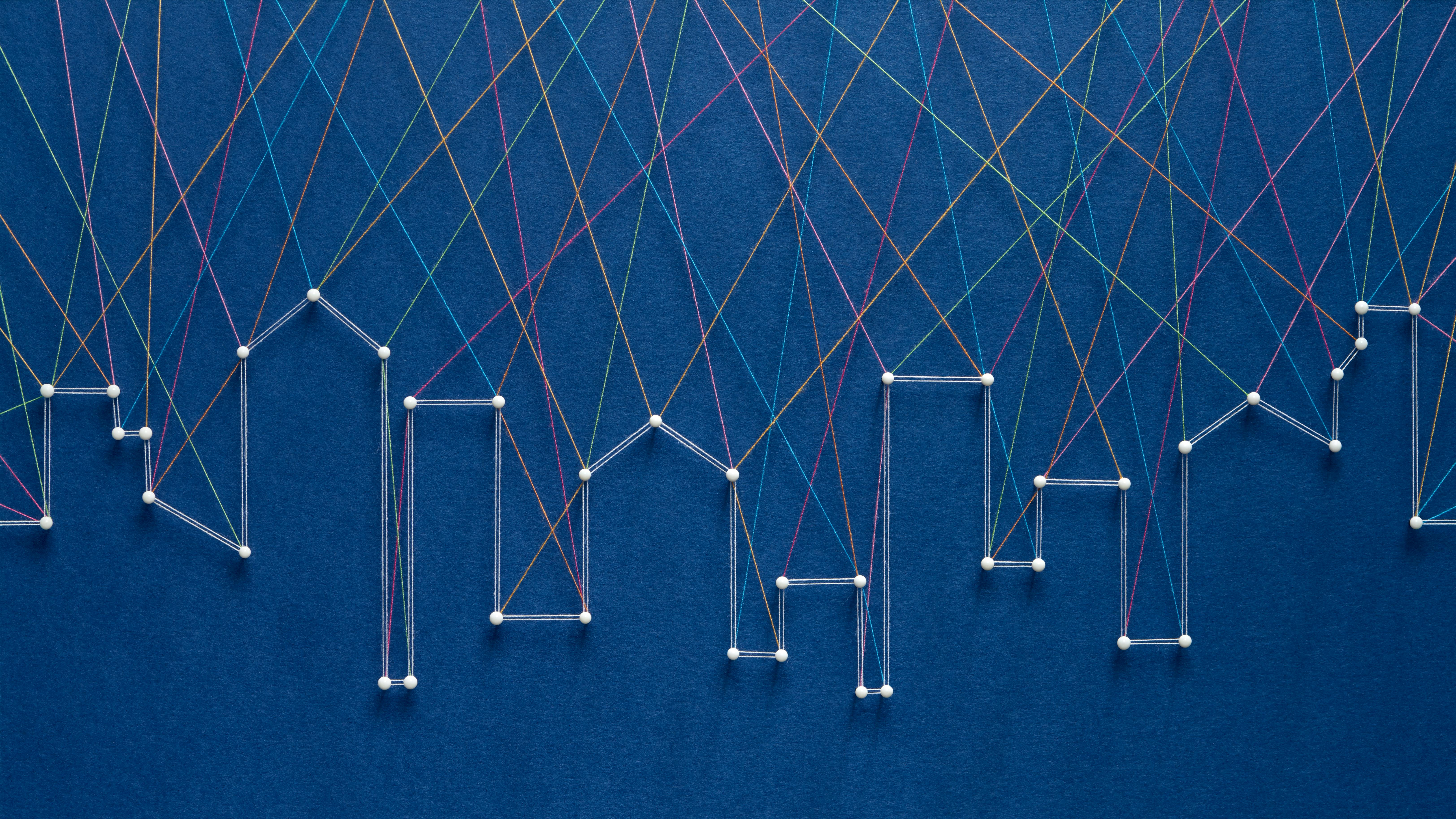 Thread art strung together with pins in the shape of a city skyline against a navy blue background.