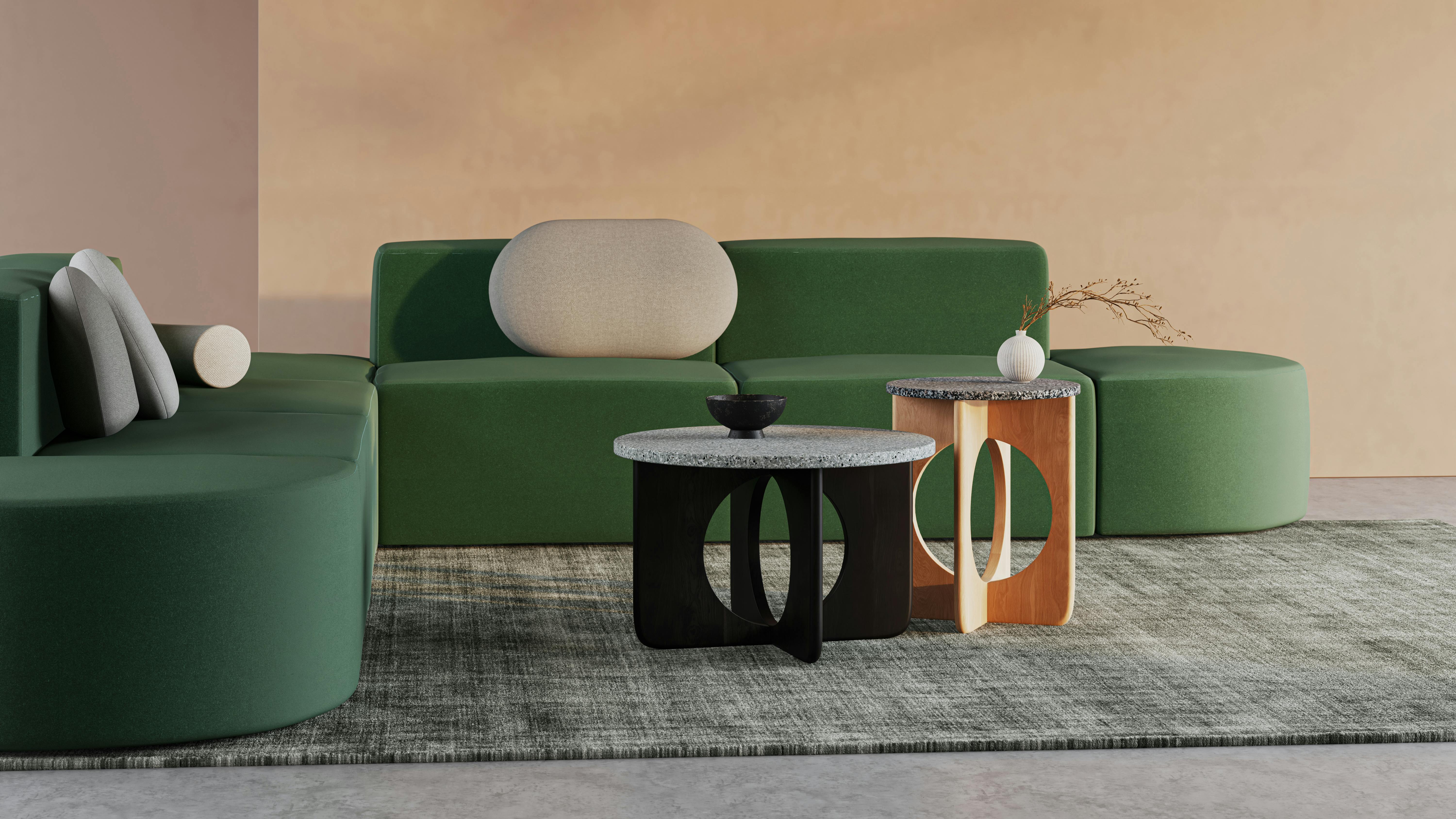 Two nesting coffee tables in front of geometric, green upholstered couch with cushions.