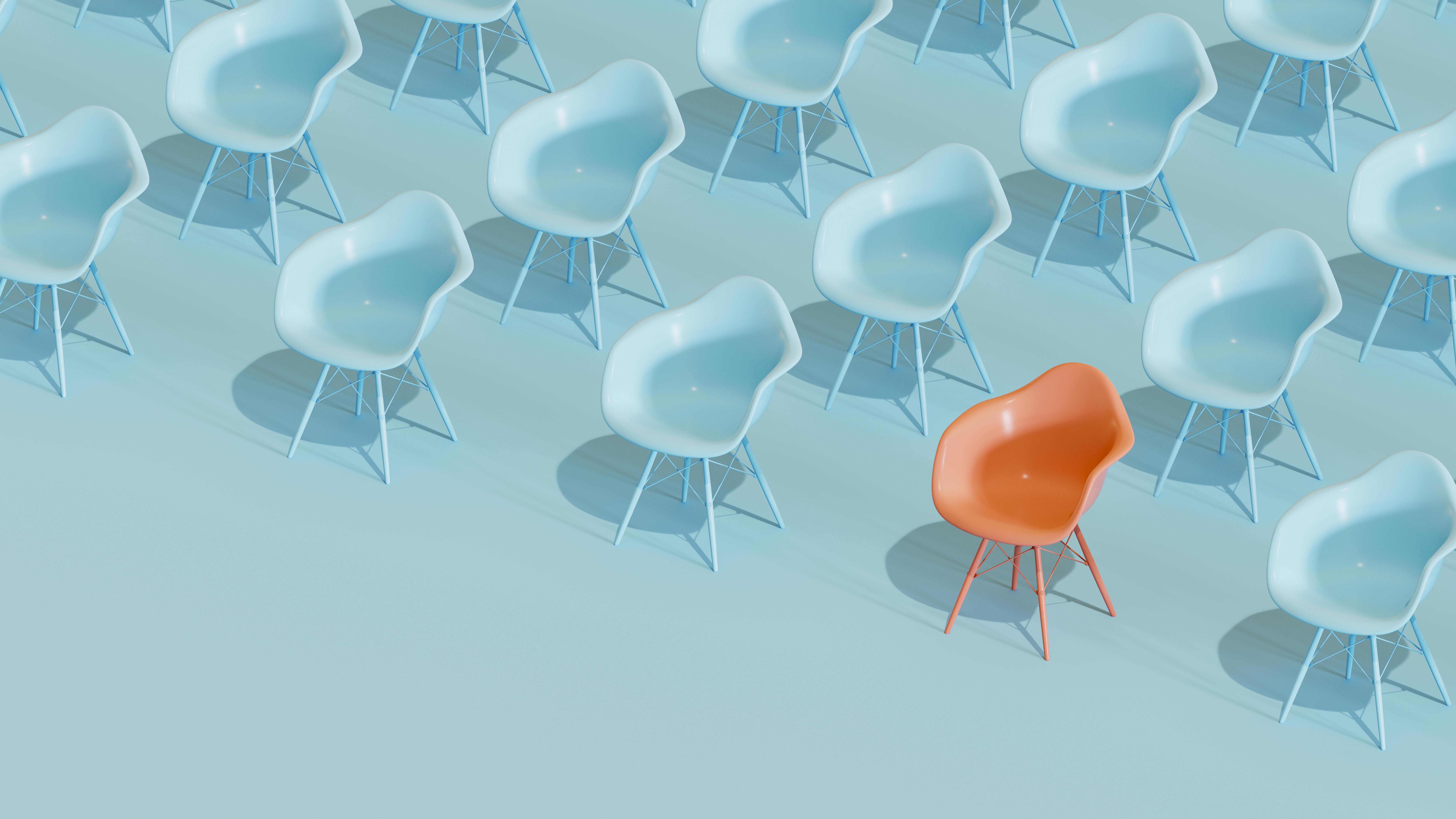 Rows of identical light blue chairs with one orange chair in first row that stands out.