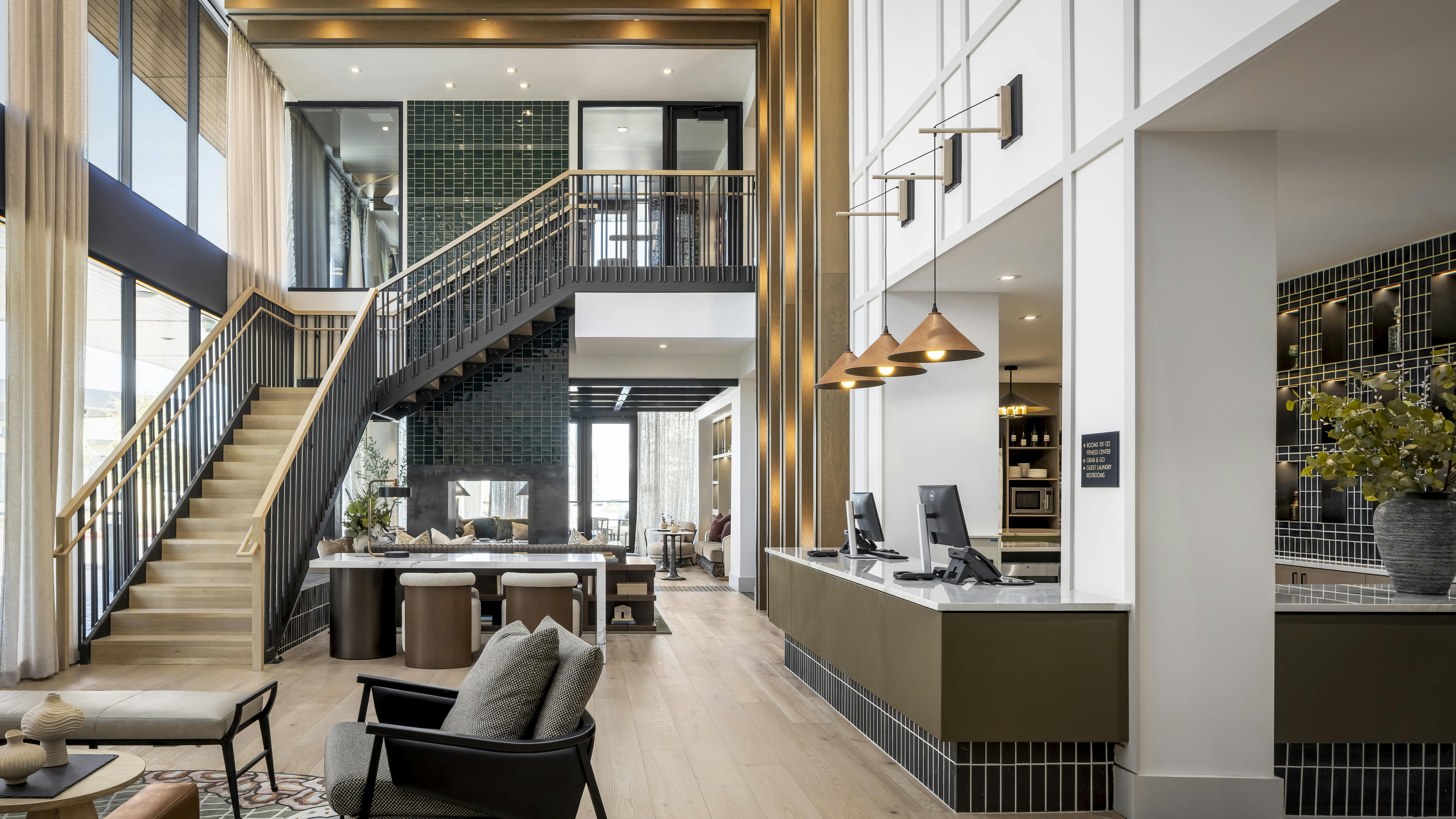 High-end hotel lobby with grand staircase, lounge furniture, and reception desk with warm tones and gold details.