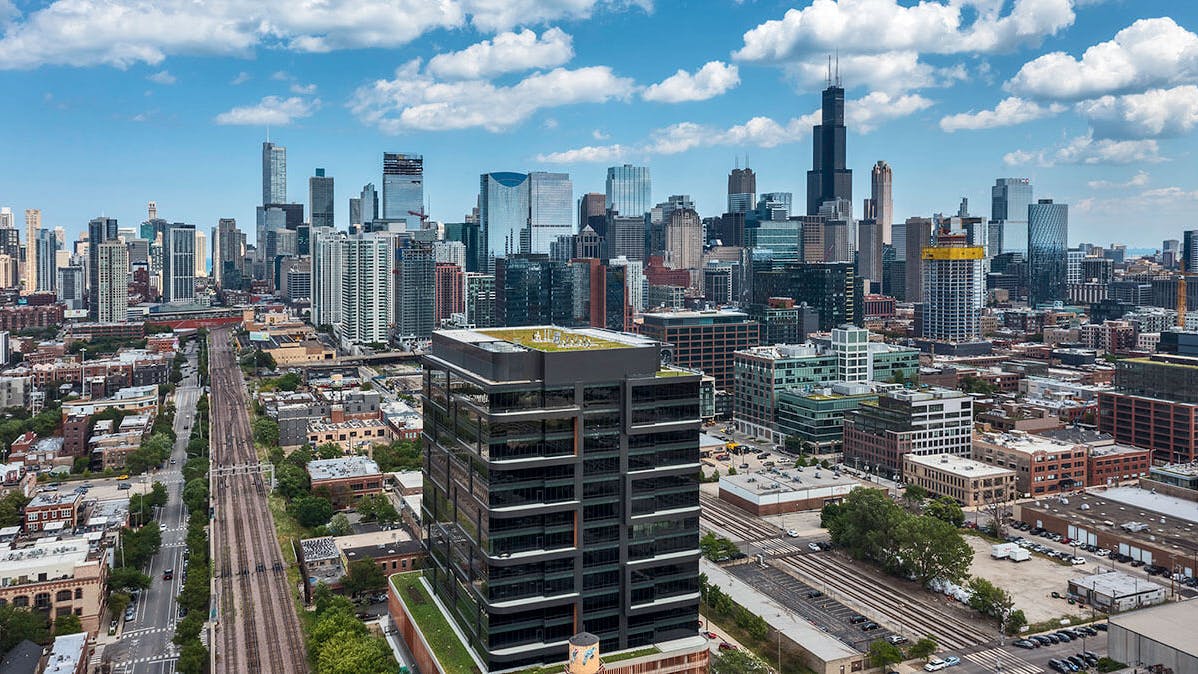 Daytime exterior view of the Fulton Labs building at 400 N Aberdeen in Chicago&rsquo;s Fulton Market district, showing its glass curtainwall facade, dark metal mullions, adjacent city skyline, and urban street frontage.