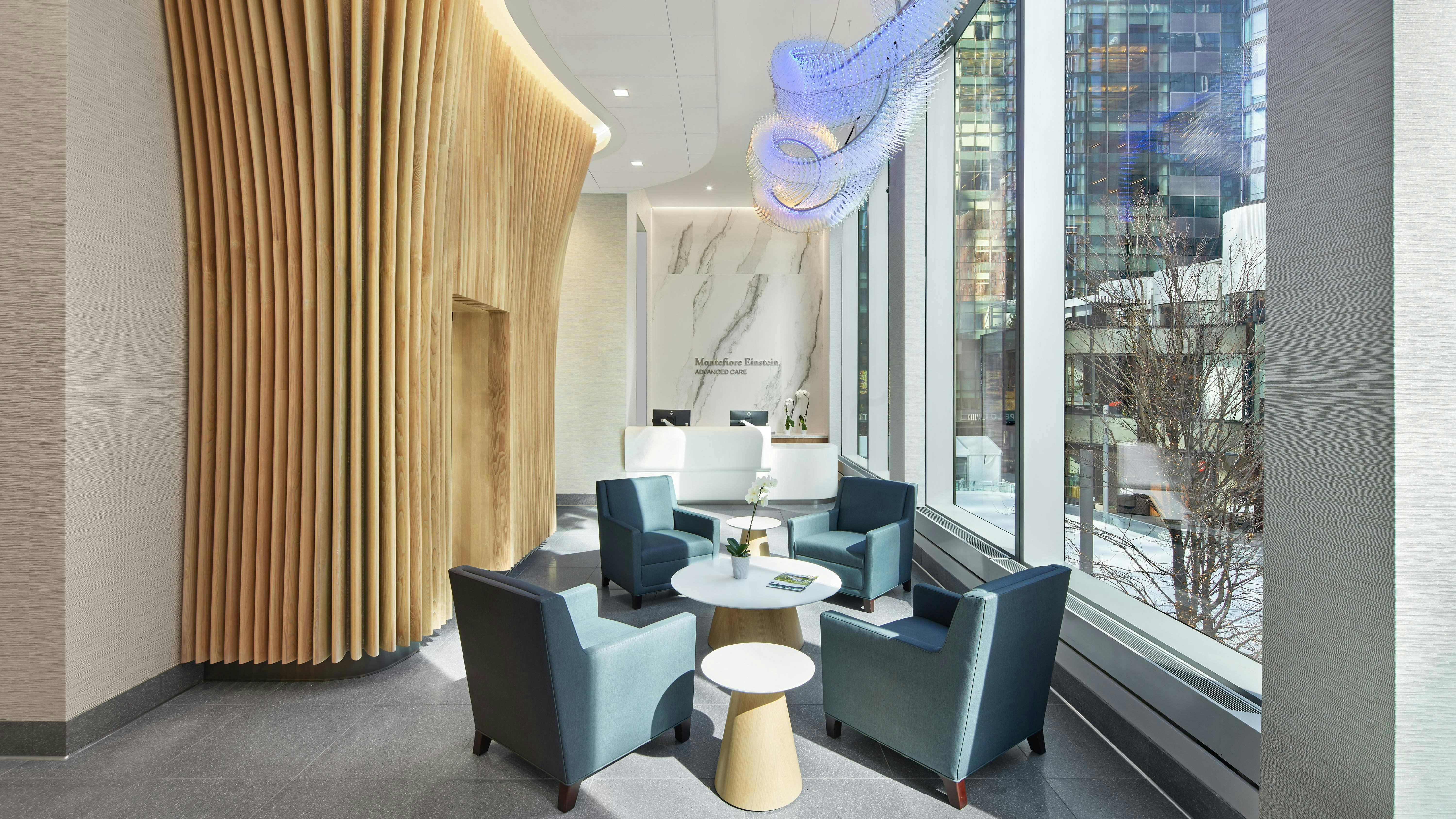 FCA Montefiore Manhattan West Entrance for healthcare facility with wood composite wall feature, bespoke light sculpture, natural daylight, and comfortable seating arrangement.