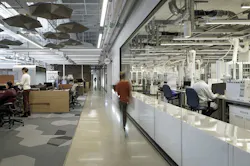 Interior view of a research and innovation center showing laboratory and office spaces connected by glass partitions, promoting visibility and collaboration. Interior view of a research and innovation center showing laboratory and office spaces connected by glass partitions, promoting visibility and collaboration.