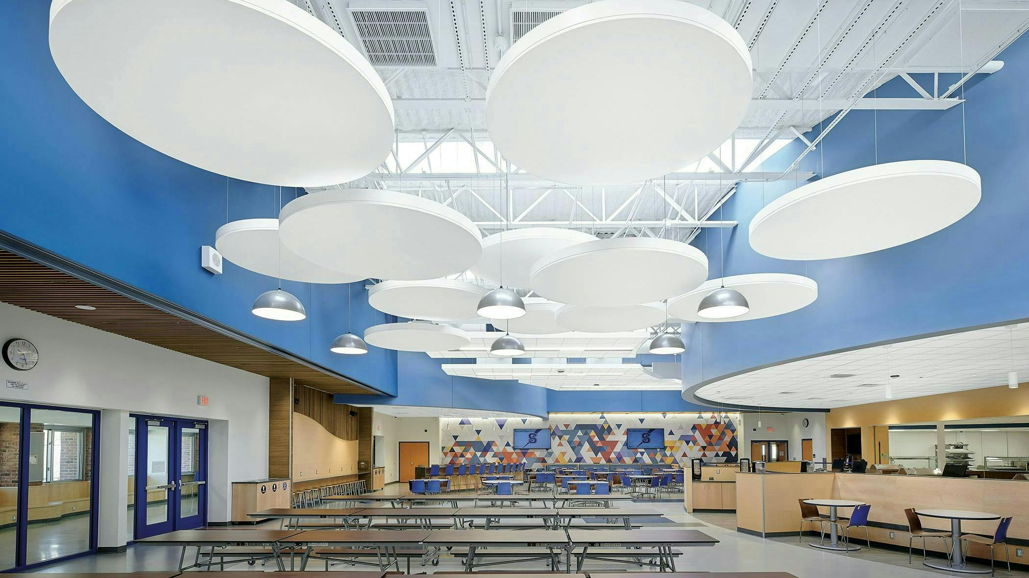 Acoustibuilt Seamless Acoustical Ceiling Clouds in white distinguish large-group seating areas against a sky-blue wall surround in the cafeteria at Saratoga Springs High School.