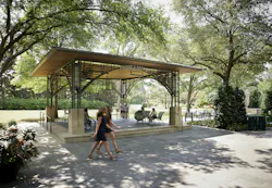 Open pavilion constructed of steel, wood, and stone with seated visitors, with gardens and greenery in the background. Open pavilion constructed of steel, wood, and stone with seated visitors, with gardens and greenery in the background.
