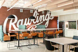 An employee gathering space and café with patterned booth seating, a tall counter with stools that mimic the look of baseball glove leather and stitching, and white acoustic ceiling fixtures and cabinetry. An employee gathering space and café with patterned booth seating, a tall counter with stools that mimic the look of baseball glove leather and stitching, and white acoustic ceiling fixtures and cabinetry.