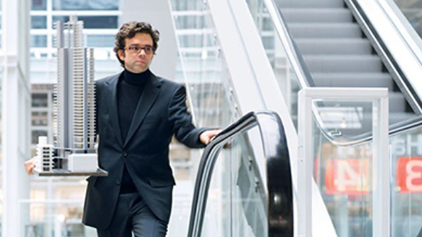 A man rides an escalator while carrying an architectural model