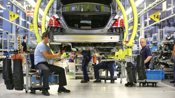 Two industrial workers assemble a car at a German factory