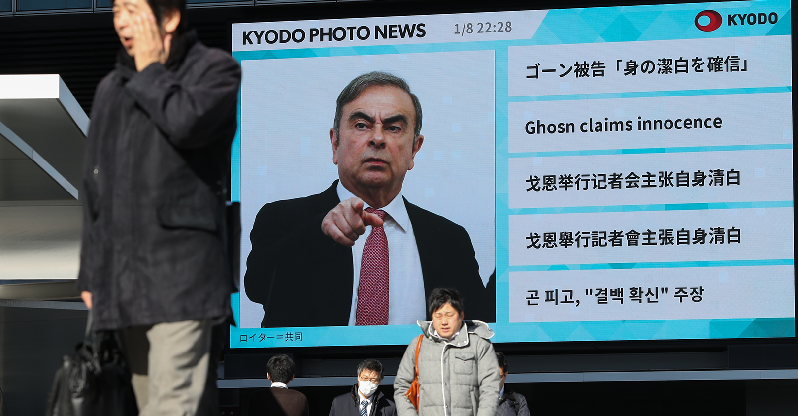 Pedestrians walk past a big screen showing images of former Nissan Motor Co. Chairman Carlos Ghosn in a news program on January 09, 2020, in Tokyo.