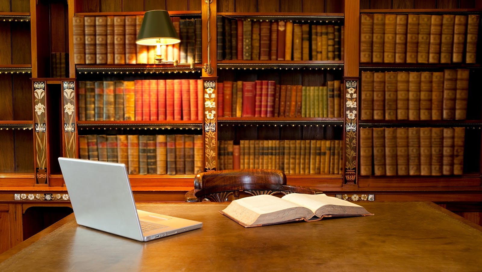 book and laptop on table with wall of books behind the table. subdued lighting